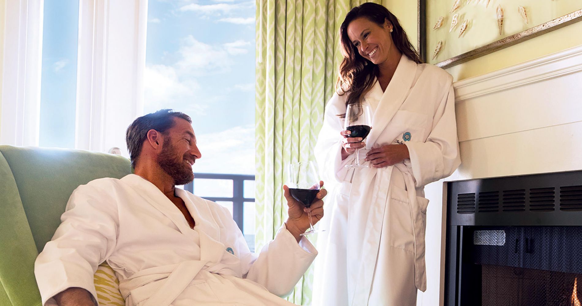 couple drink wine in bathrobes by a roaring fire