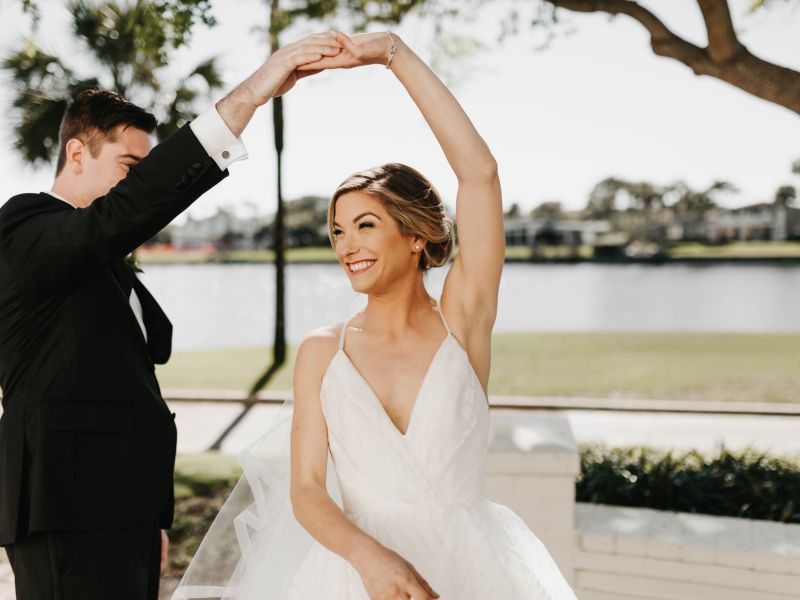 A groom twirls his bride under a tree with the lagoon in the background at Ponte Vedra Inn & Club