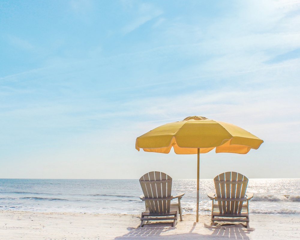 two beach chairs with yellow umbrella along ocean coast