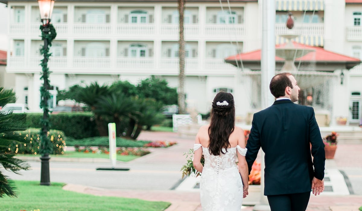 A bride and groom walk down a stone pathway towards the Historic Inn Building at Ponte Vedra Inn & Club