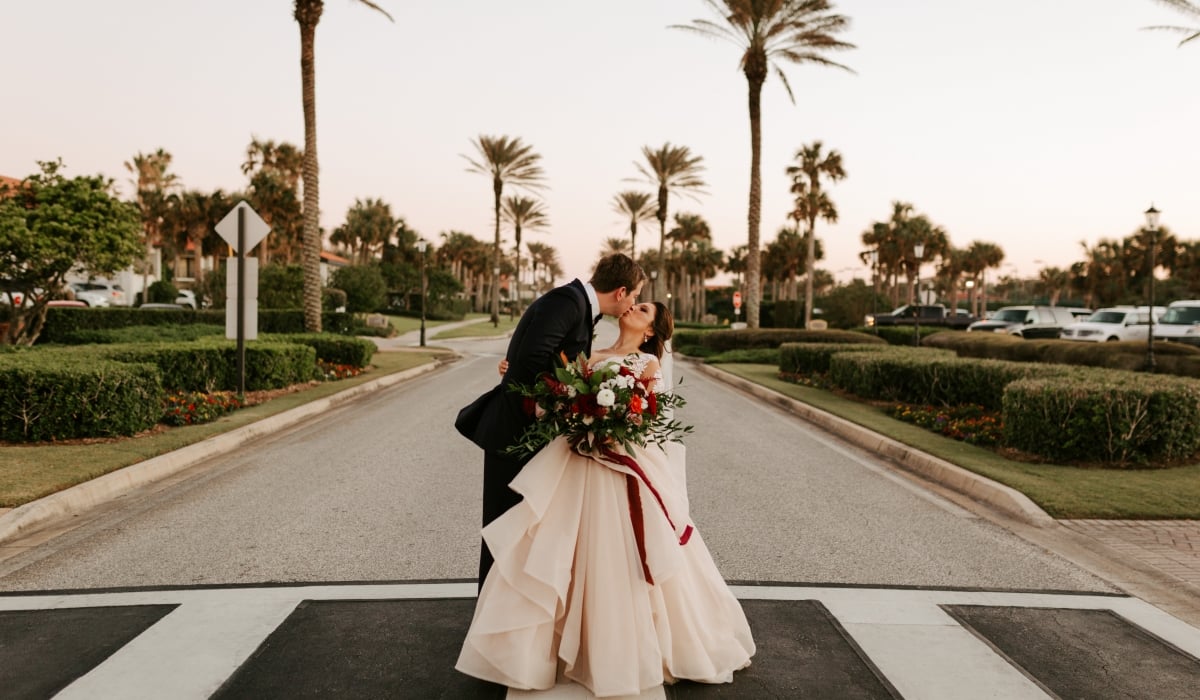 A bride and groom kiss in the street framed by palm trees at Ponte Vedra Inn & Club.