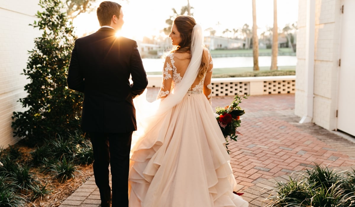 A shot from the back as a bride and groom walk down a stone pathway towards the lagoon at sunset at Ponte Vedra Inn & Club.