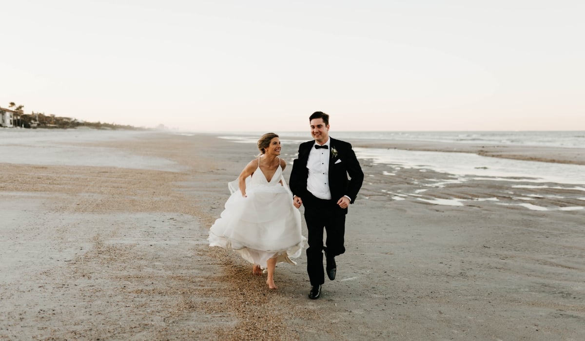 A bride and groom run along the beach at Ponte Vedra Inn & Club.