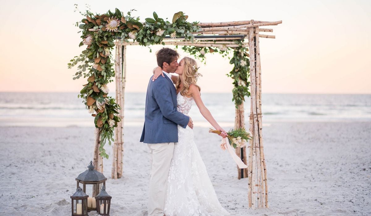 A bride and groom kiss under an arbor on the beach at Ponte Vedra Inn & Club.
