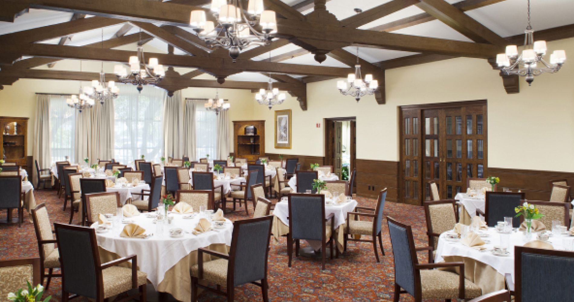 Tables set under the exposed wood beams and chandeliers of the Inn Dining Room at Ponte Vedra Inn & Club.