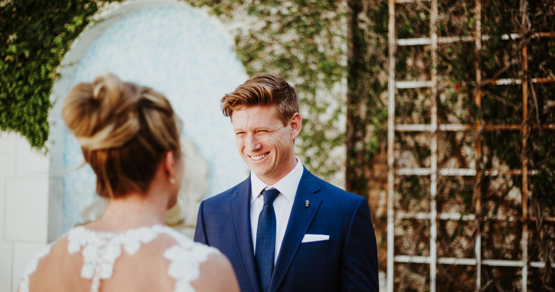 groom smiles at bride next to trellis
