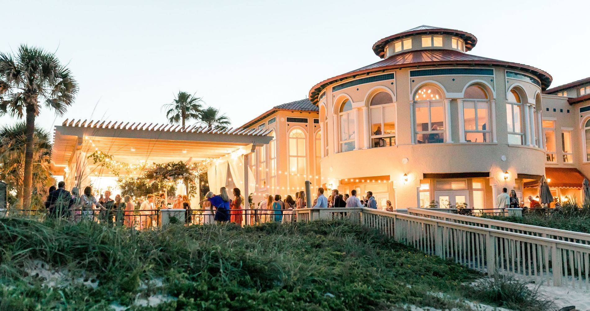 Exterior image of building and trellis at night with string lights. 
