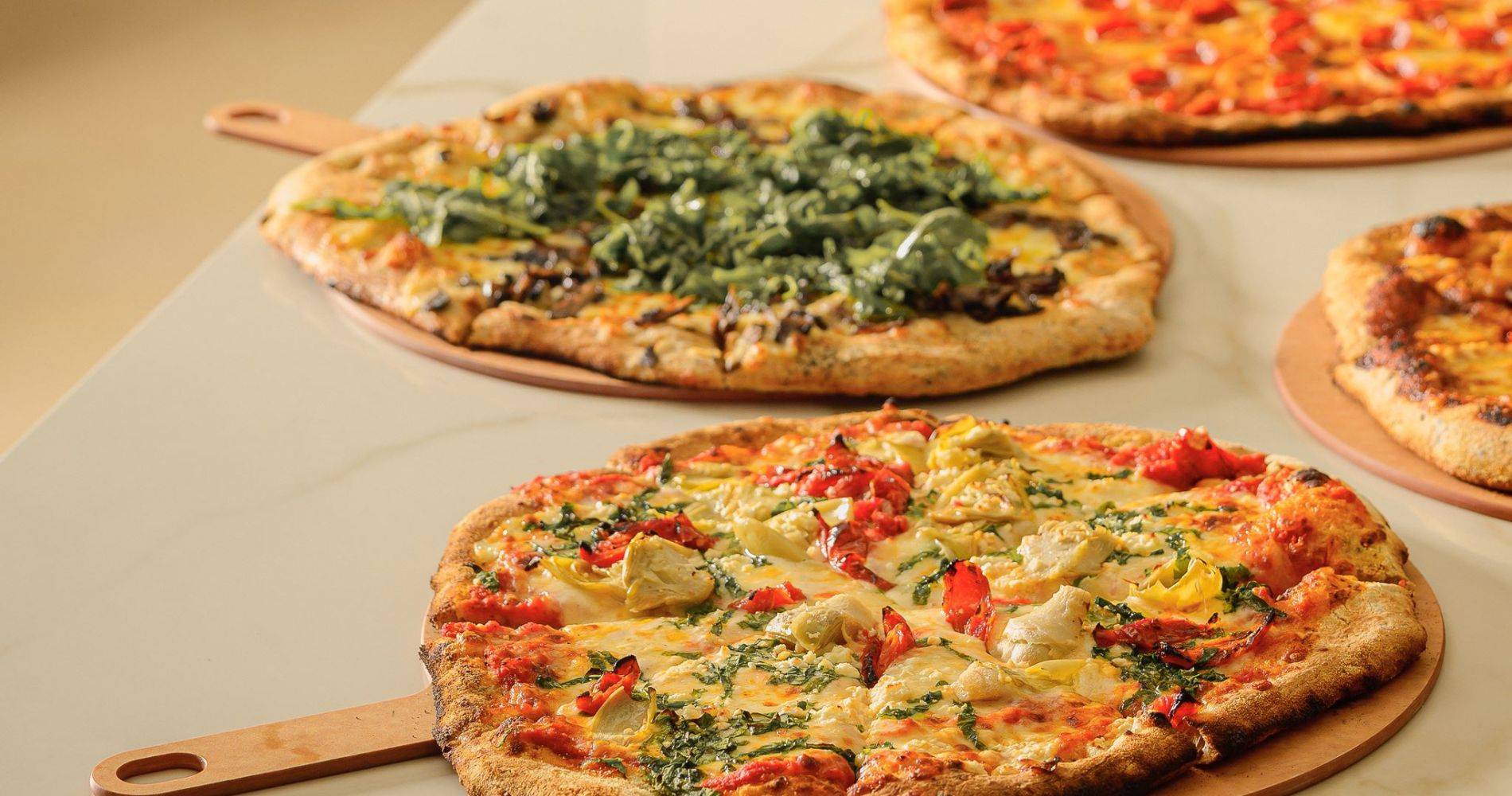 four freshly made pizzas on a counter