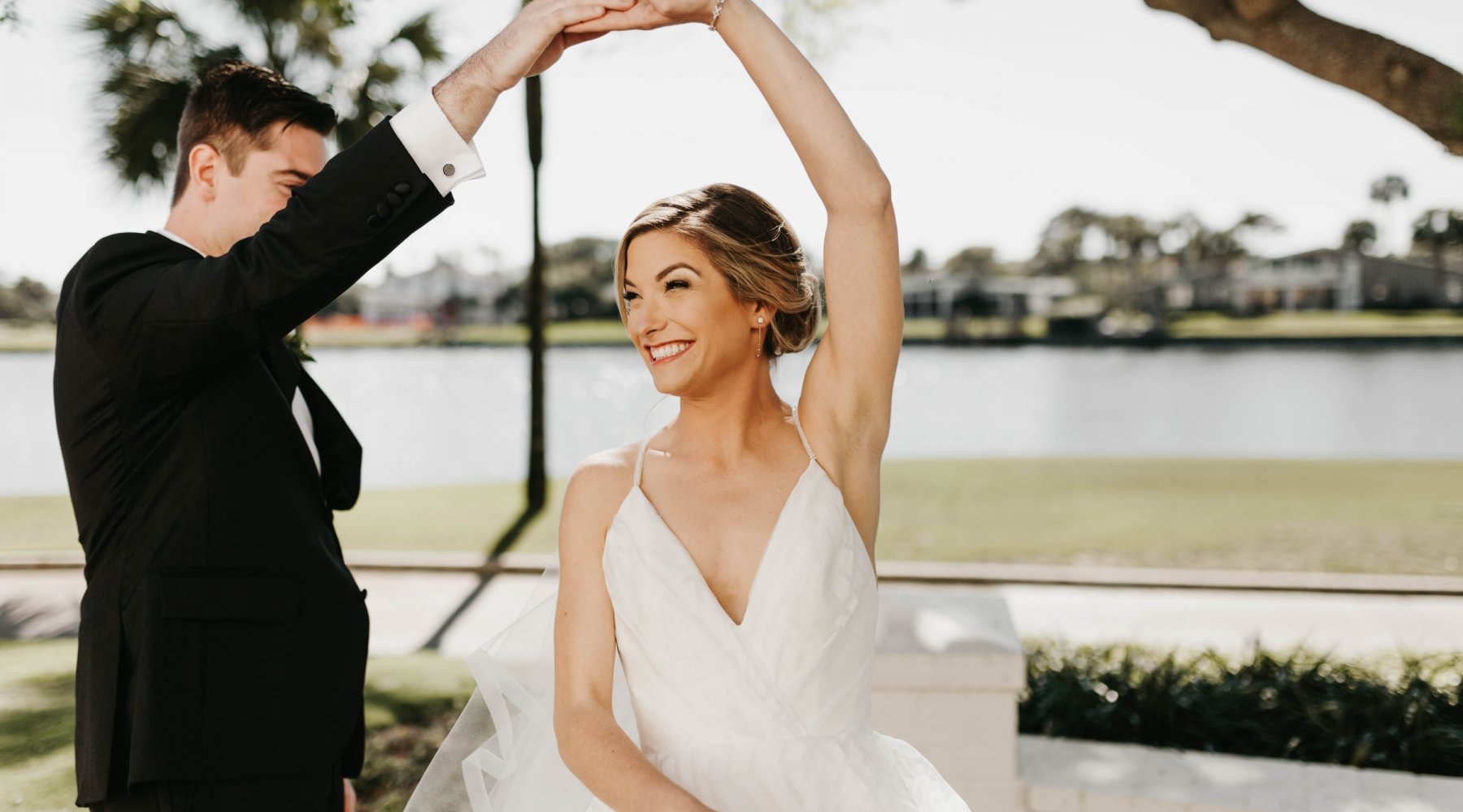 A groom twirls his bride under a tree with the lagoon in the background at Ponte Vedra Inn & Club