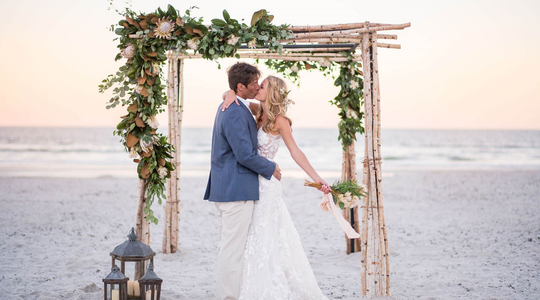 A bride and groom kiss under an arbor on the beach at Ponte Vedra Inn & Club.
